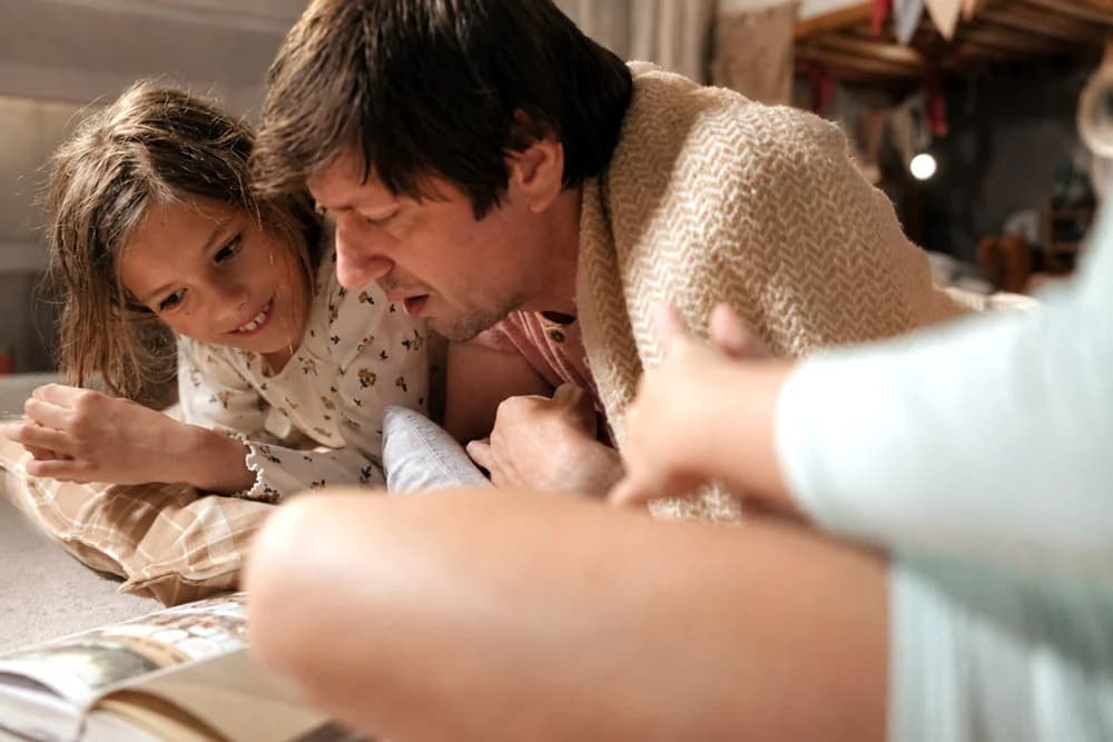 A father and daughter lying on the floor, reading one book together