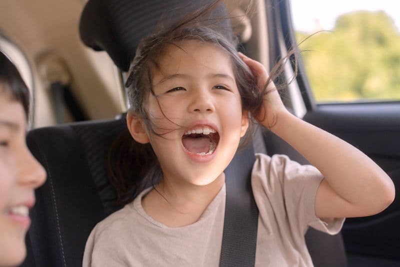 A child laughing in the back seat of a car