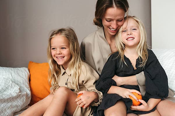 A mother laughing with her two daughters on a sofa